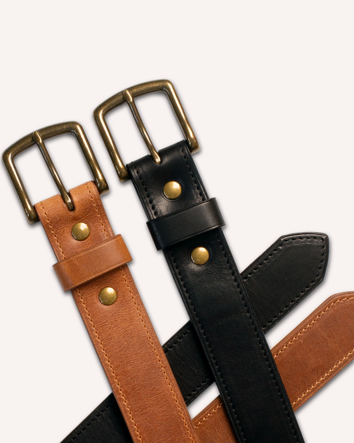 Two Heirloom Belts from Archive Leather Goods, in Natural and Black Horween Dublin leather, crossed over each other.