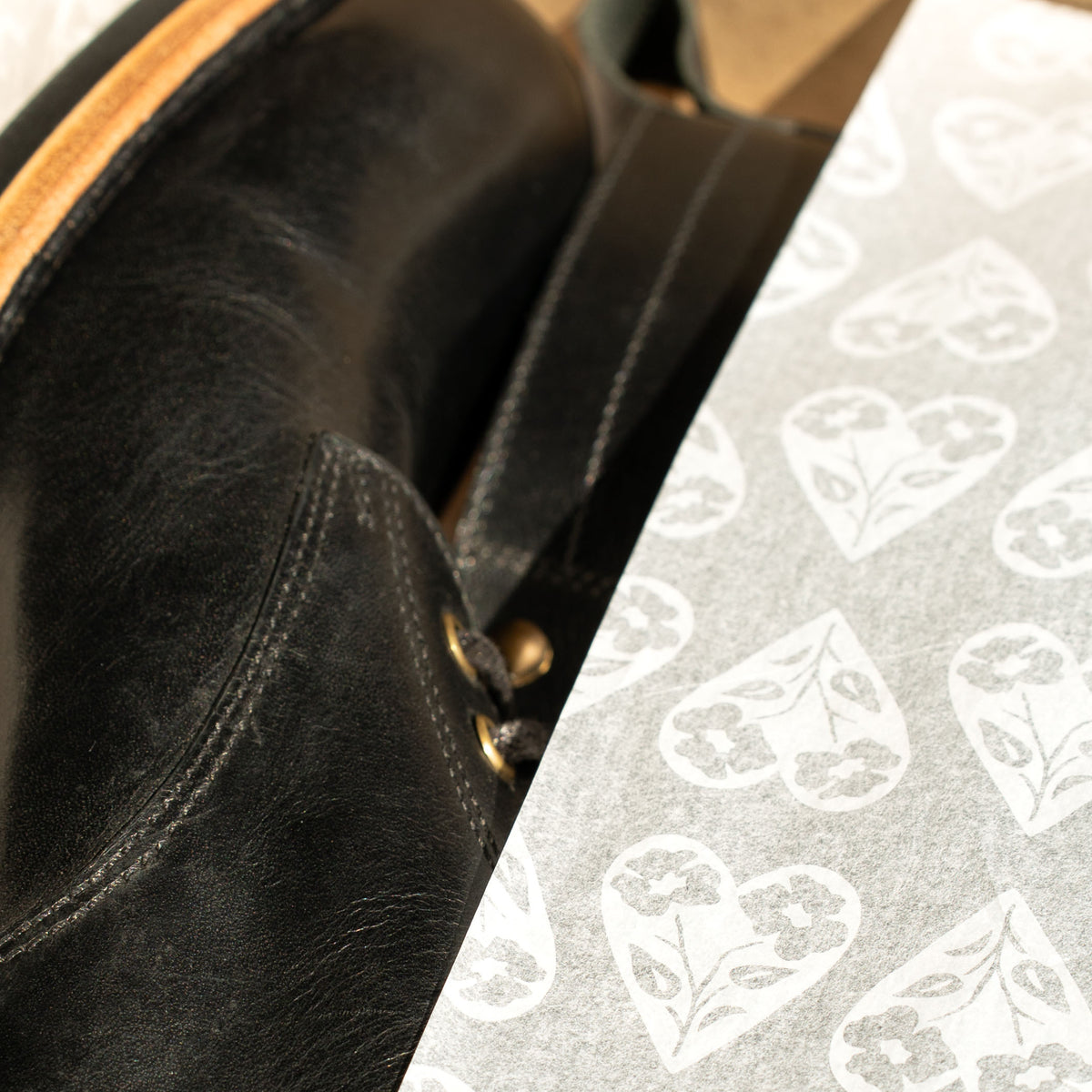 A black boot wrapped in tissue paper printed with the Archive heart.