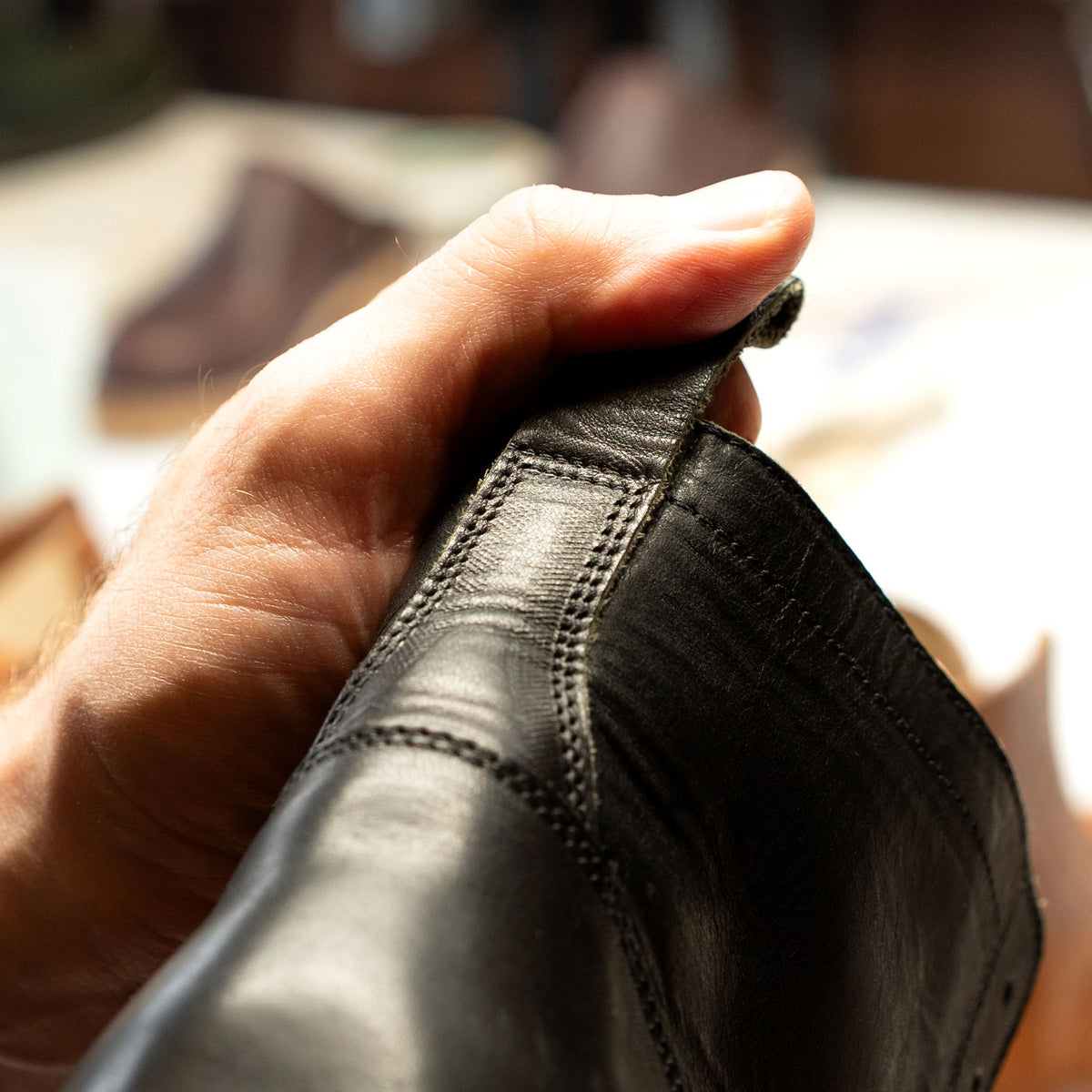 A hand holding a black boot up for final inspection.