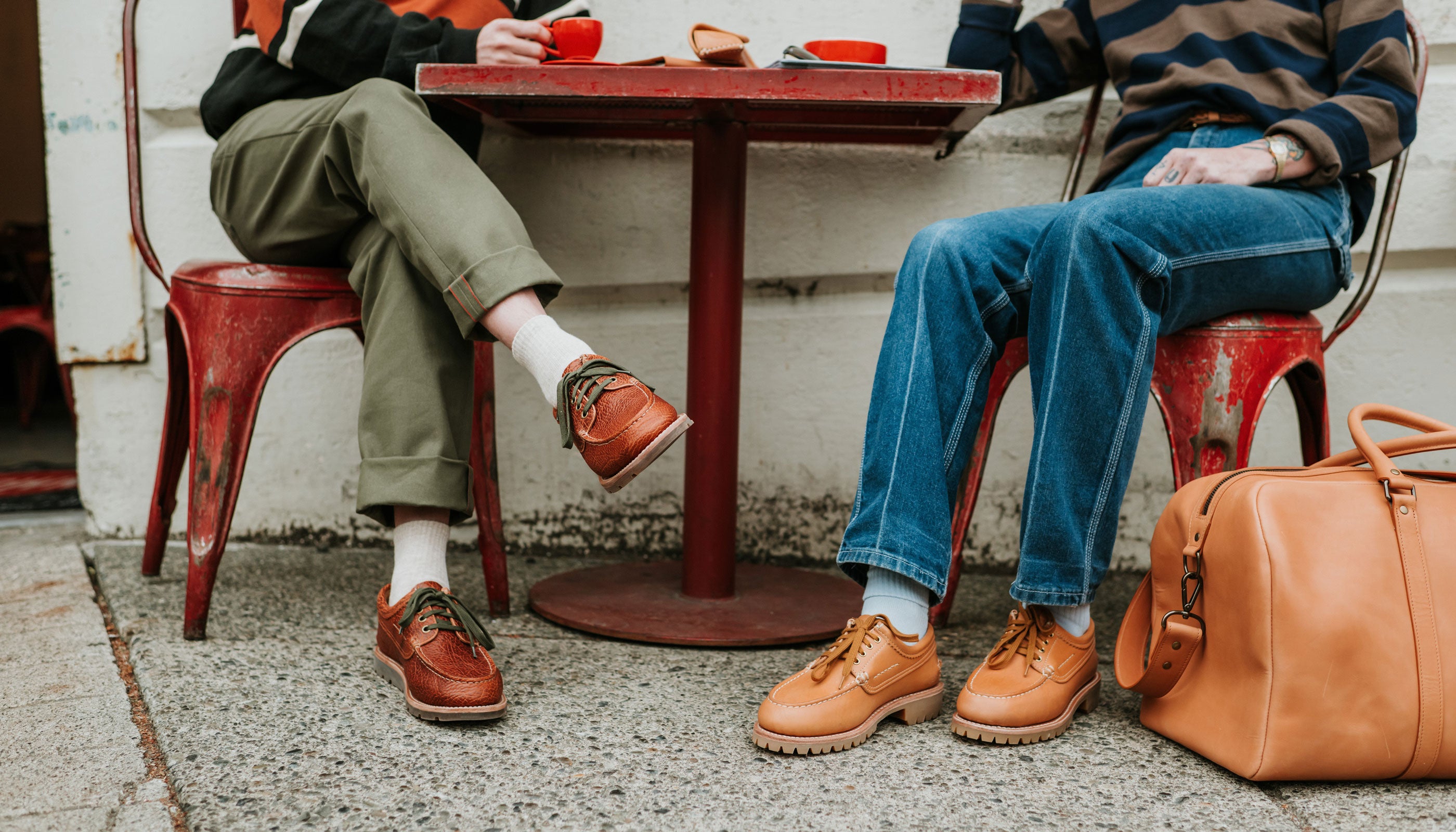 Two people sitting at a red table outdoors, wearing moc-toed shoes.