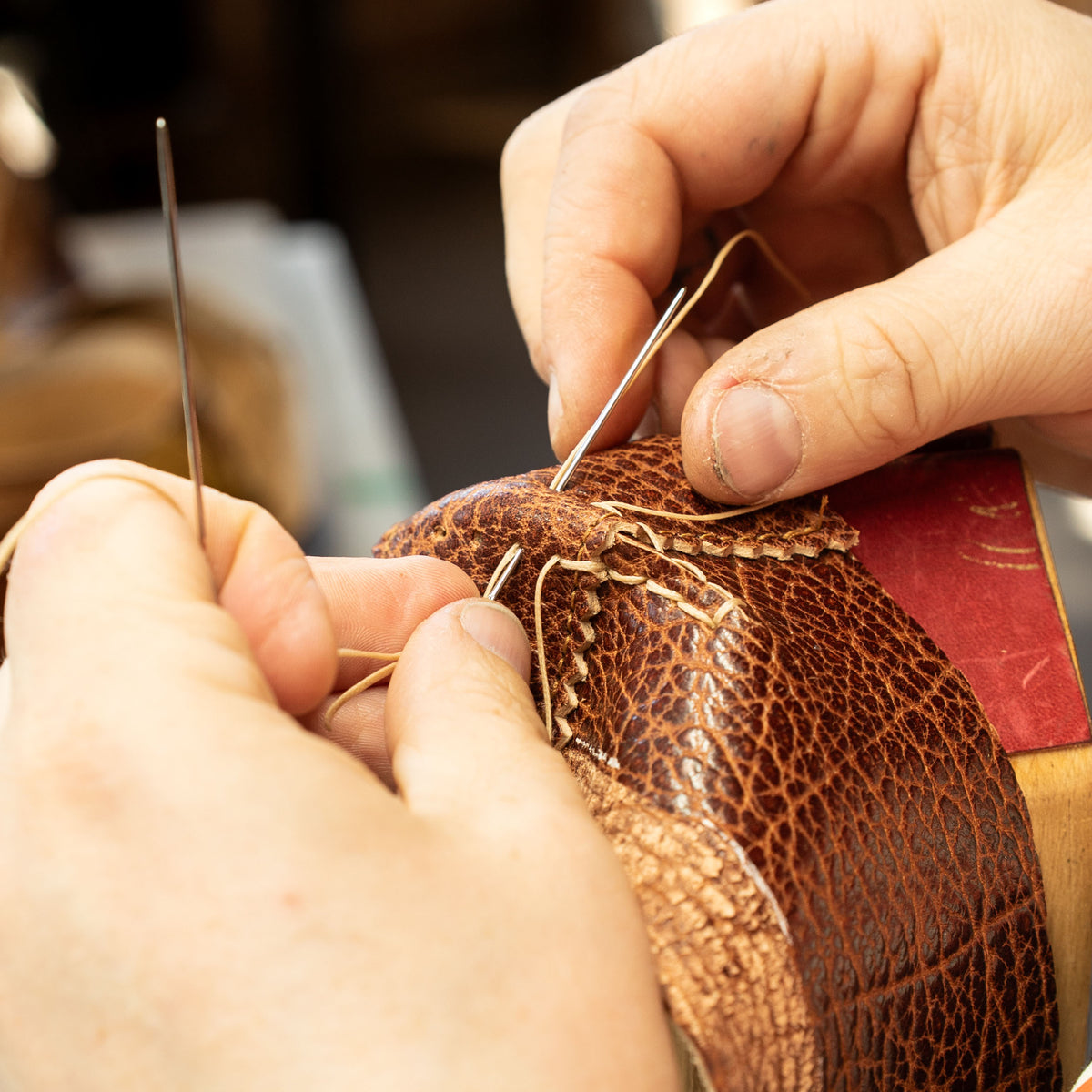 Hands stitching horsehide leather with two needles.