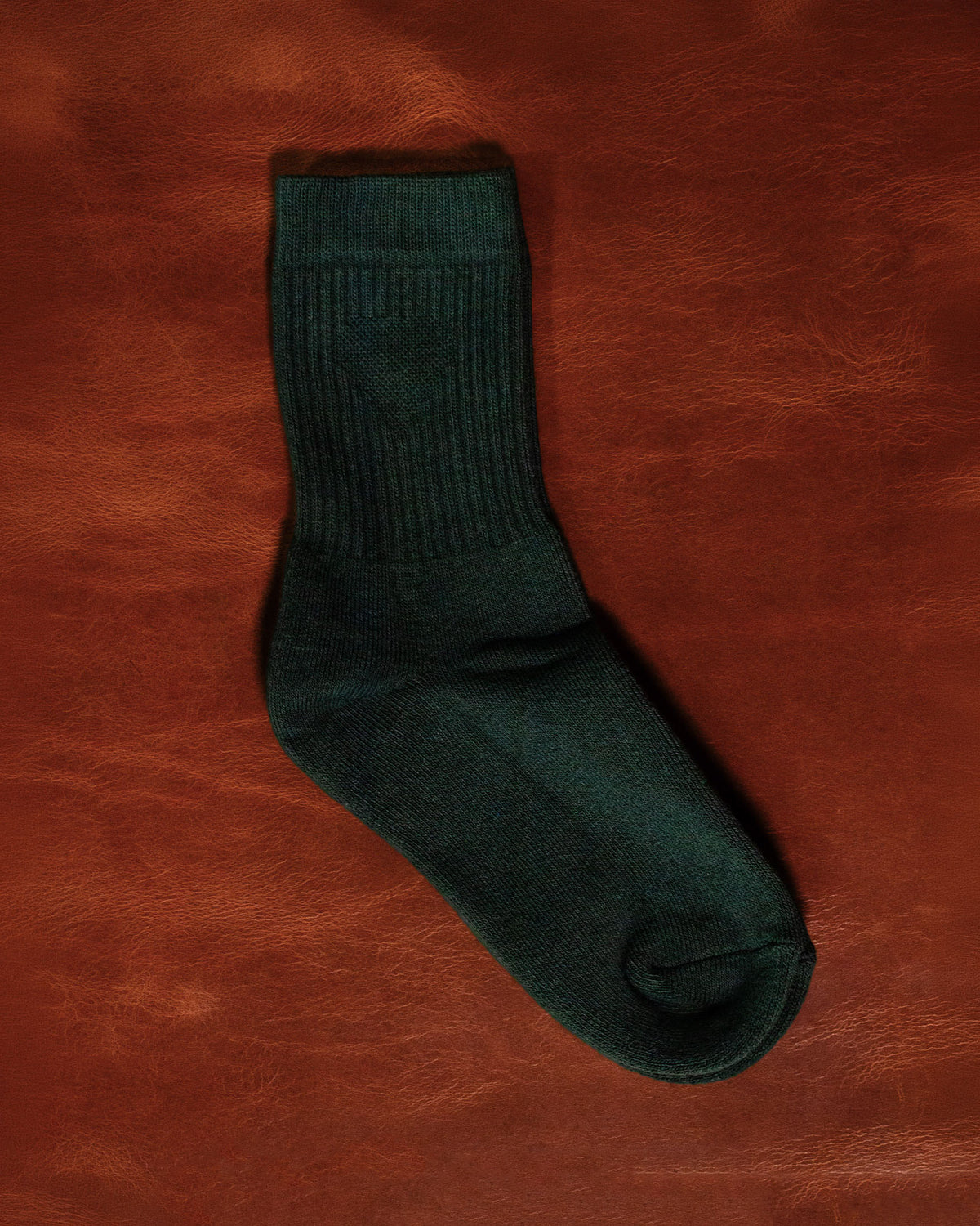 A pair of Foundation Socks from Archive Leather Goods in Salal (green), laid flat on a leather background.