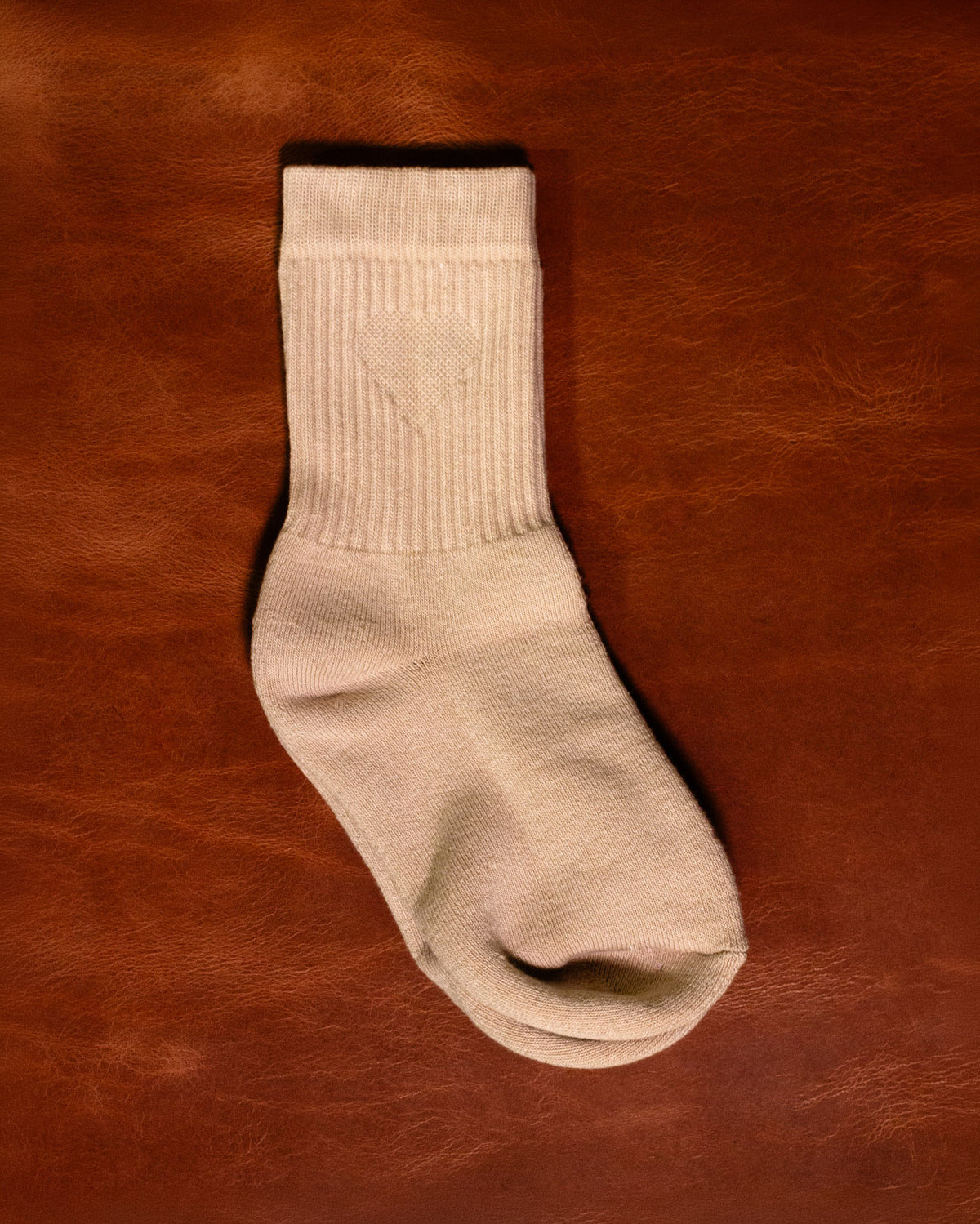 A pair of Foundation Socks from Archive Leather Goods in Driftwood (natural), laid flat on a leather background.