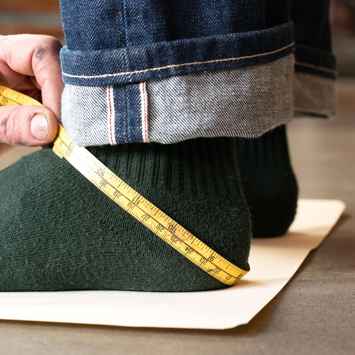 A foot in a green sock being measured with a tape measure on a sizing sheet.