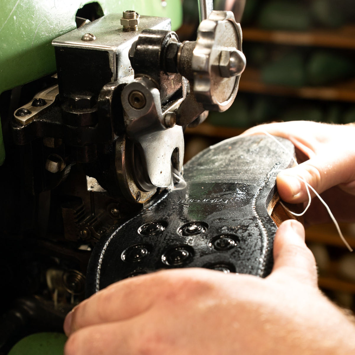 Hands guiding a boot sole through a stitching machine.